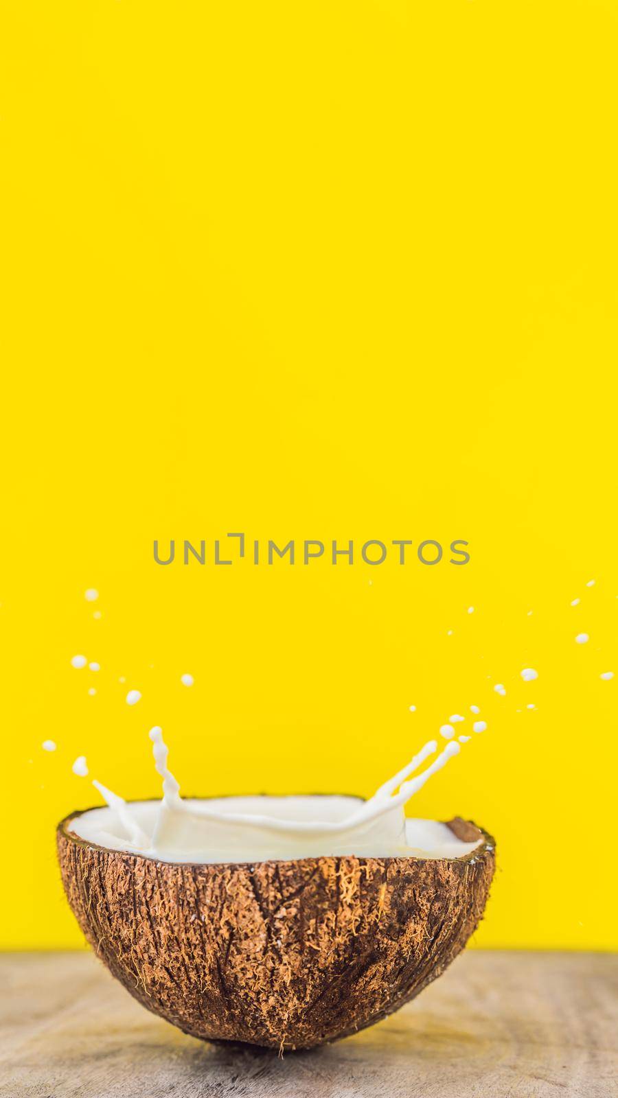 Coconut fruit and milk splash inside it on yellow background VERTICAL FORMAT for Instagram mobile story or stories size. Mobile wallpaper by galitskaya