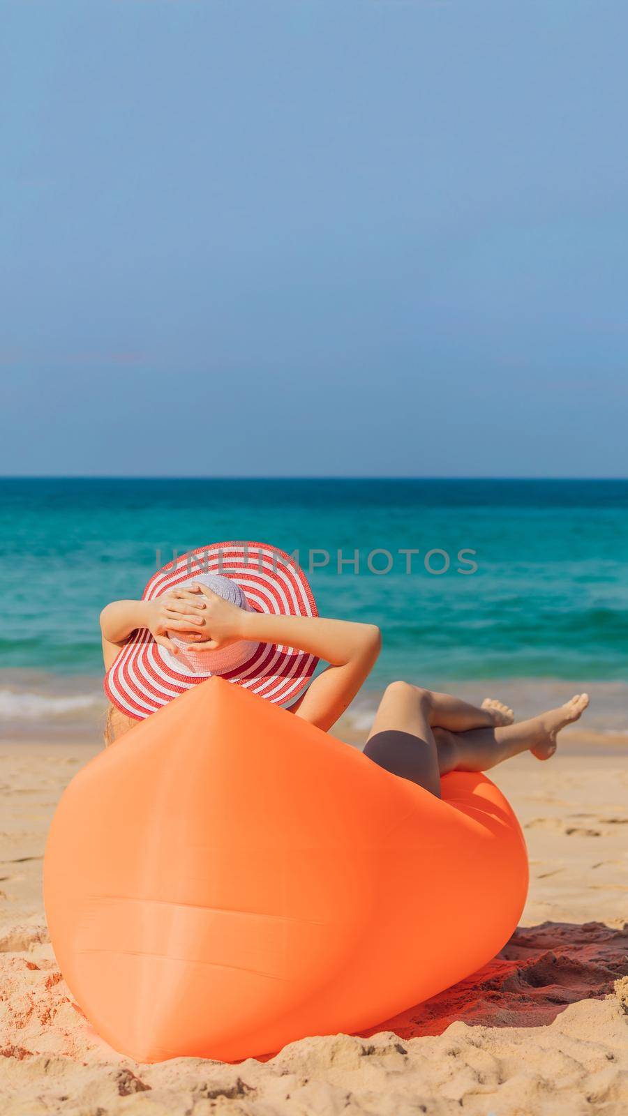 Summer lifestyle portrait of pretty girl sitting on the orange inflatable sofa on the beach of tropical island. Relaxing and enjoying life on air bed VERTICAL FORMAT for Instagram mobile story or stories size. Mobile wallpaper by galitskaya