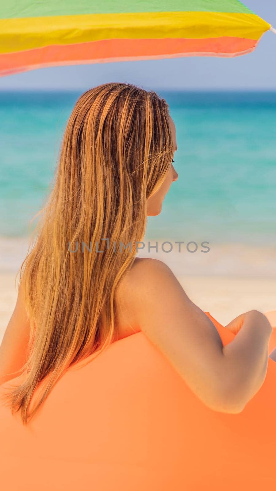 Summer lifestyle portrait of pretty girl sitting on the orange inflatable sofa on the beach of tropical island. Relaxing and enjoying life on air bed. VERTICAL FORMAT for Instagram mobile story or stories size. Mobile wallpaper