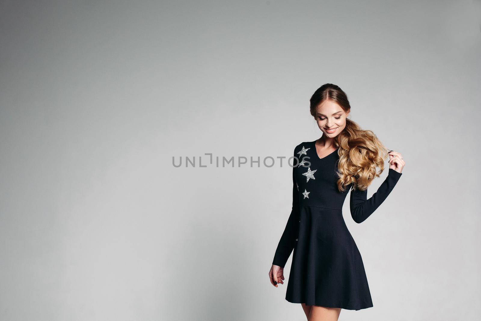 Portrait of beautiful positivity woman with long curly hair and shining eyes, wearing in fashionable black dress with stars, jumping in grey studio. Stylish woman dancing and smiling.