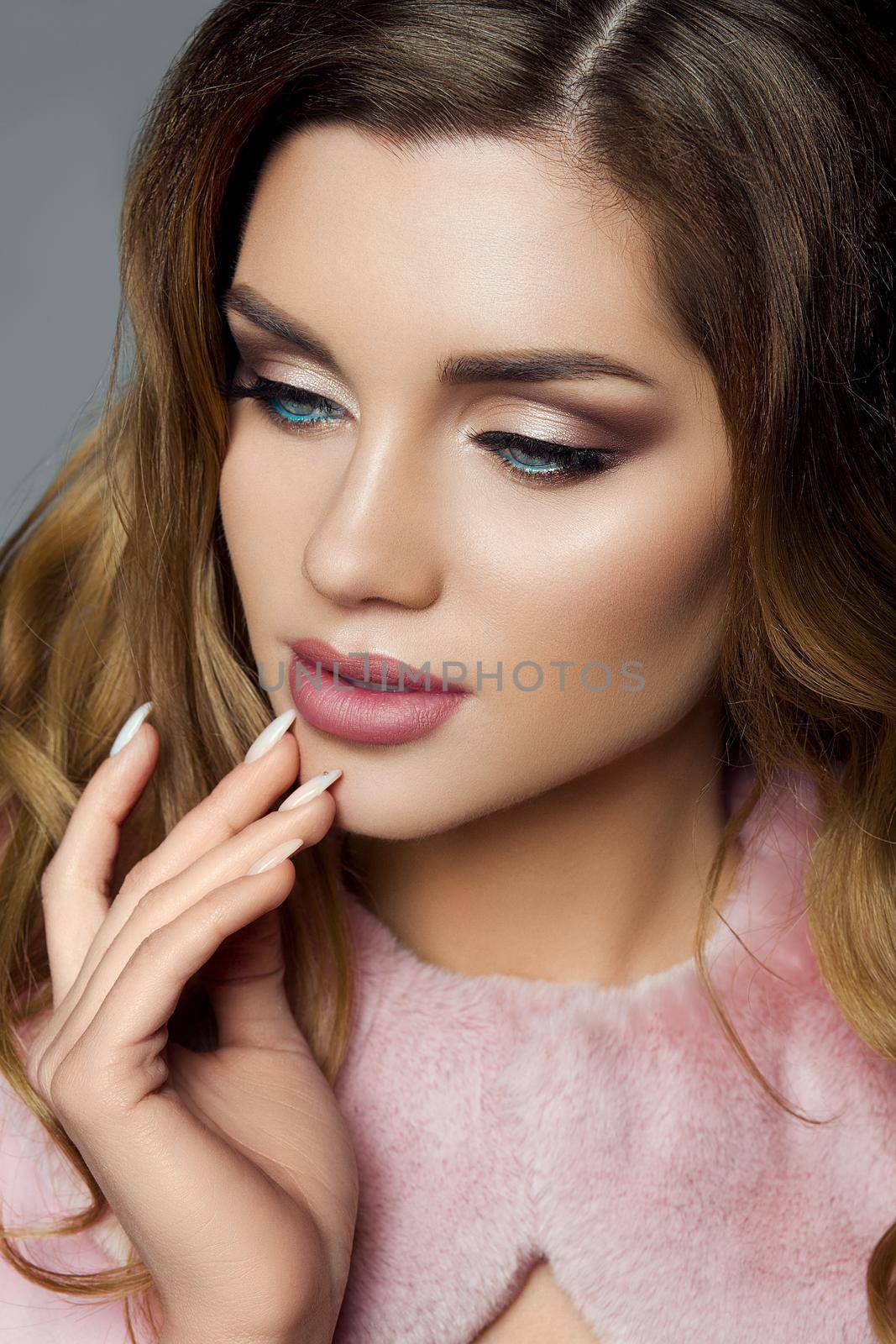 Beautiful woman in pink blouse with volumed hairstyle, bronze sunburn and clear face skin touching lips by hand. Perfect make up, plump lips and clasic manicure. Concept of beauty and cosmetic.