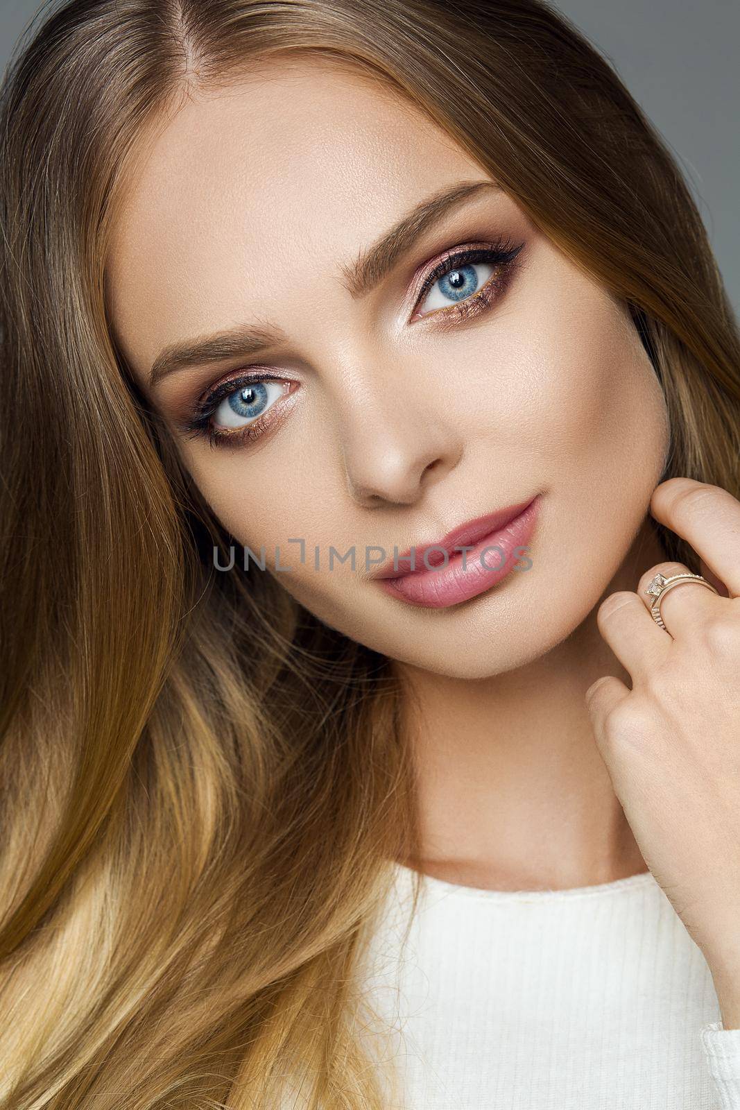 Close-up of pretty girl with fair hair and professional natural make-up looking at camera calmly.