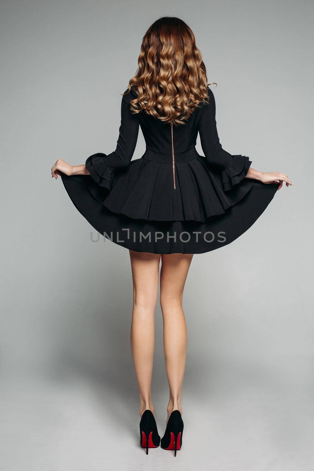 Brunette model with wavy hair posing in beautiful black dress with flounced skirt and high heels. by StudioLucky