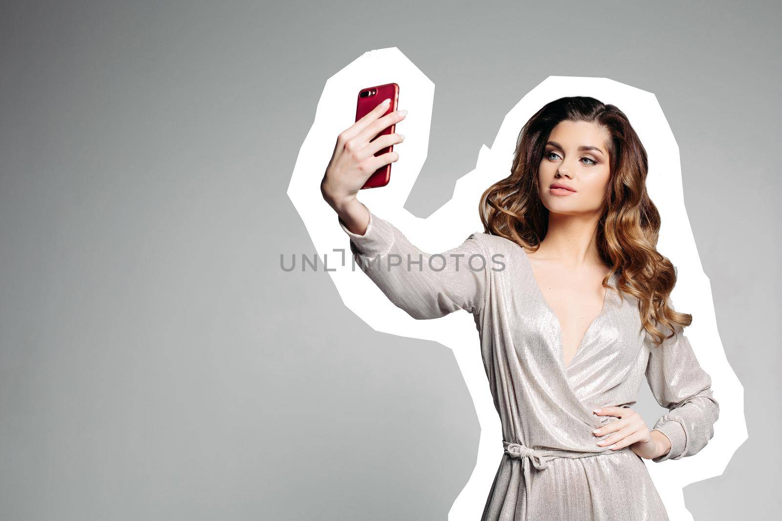 View of serious and pretty brunette girl with plump lips, wearing in silver dress, holding cell phone, smiling and taking photo. Attractive woman posing making self portrait. Comics effect.