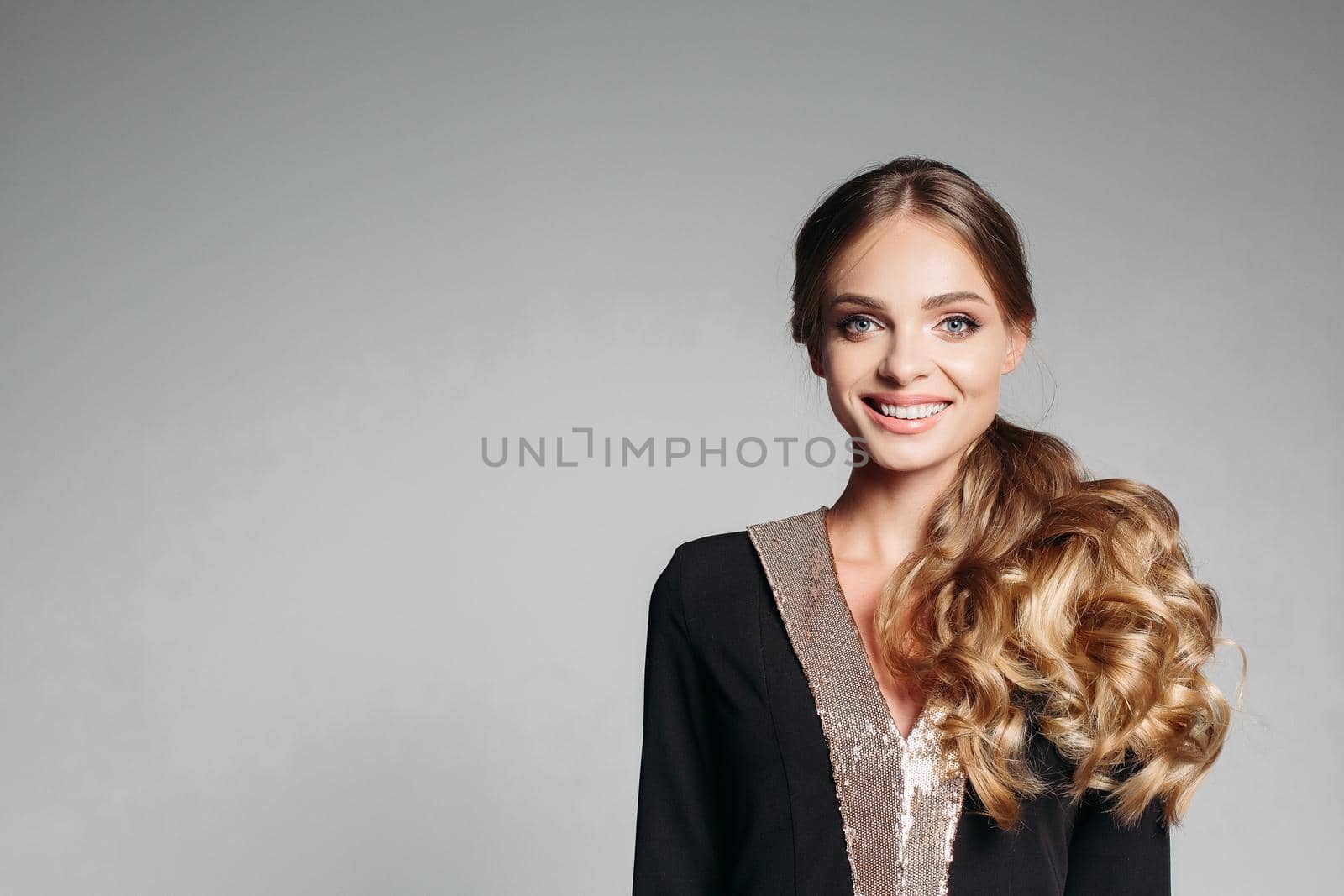 Beautiful, sweet blonde with wavy hair, in an elegant designer suit. Friendly, smiling happily. Look at the camera Isolate on a gray background