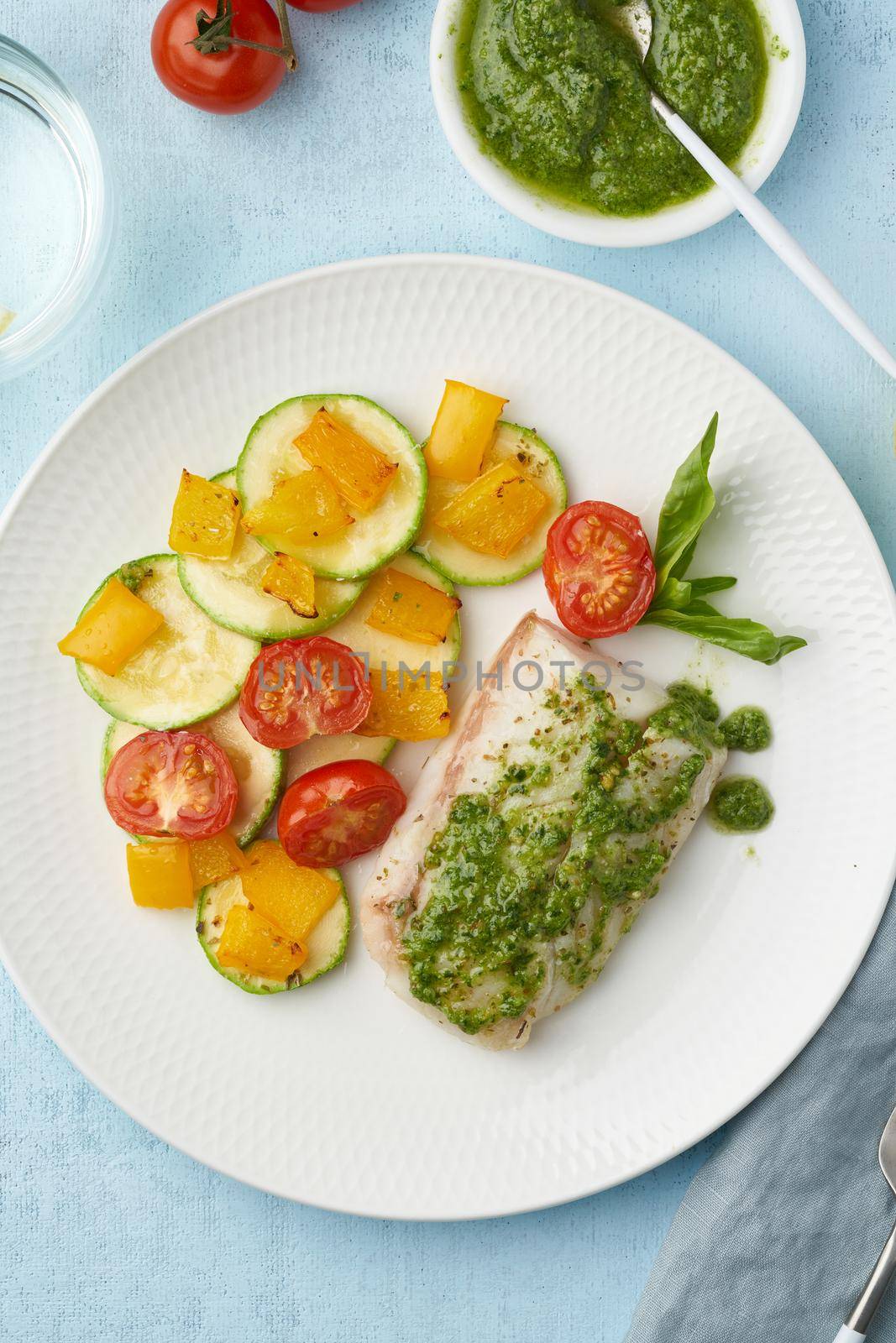 Keto dinner with white fish. Oven baked fillet of cod, pike perch with vegetables and pesto sauce. Healthy diet food, ketogenic paleo diet, Mediterranean cuisine. Blue background. Top view, vertical