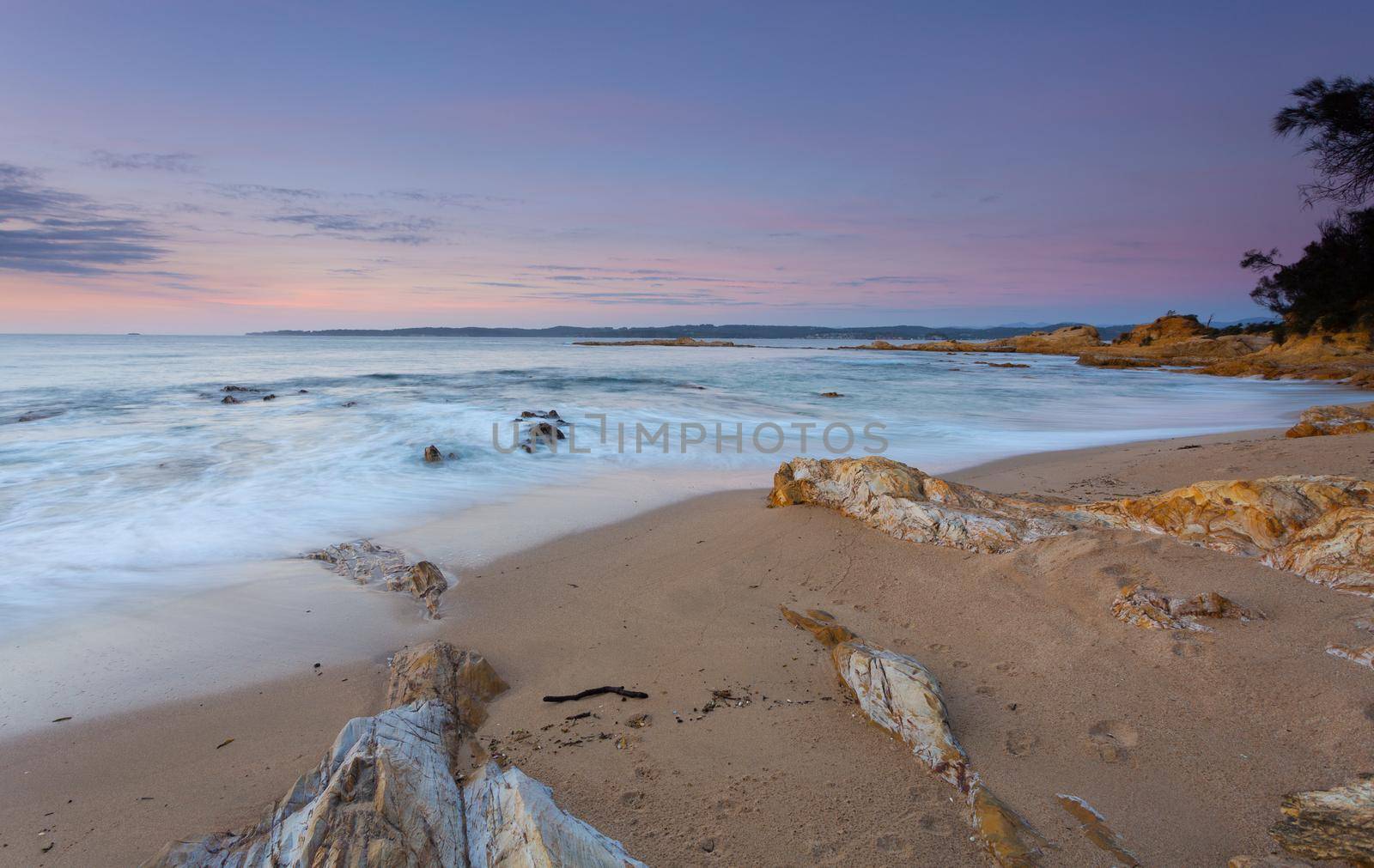 Waves gently lap the beach in the dawn morning light on a quiet beach in NSW Australia