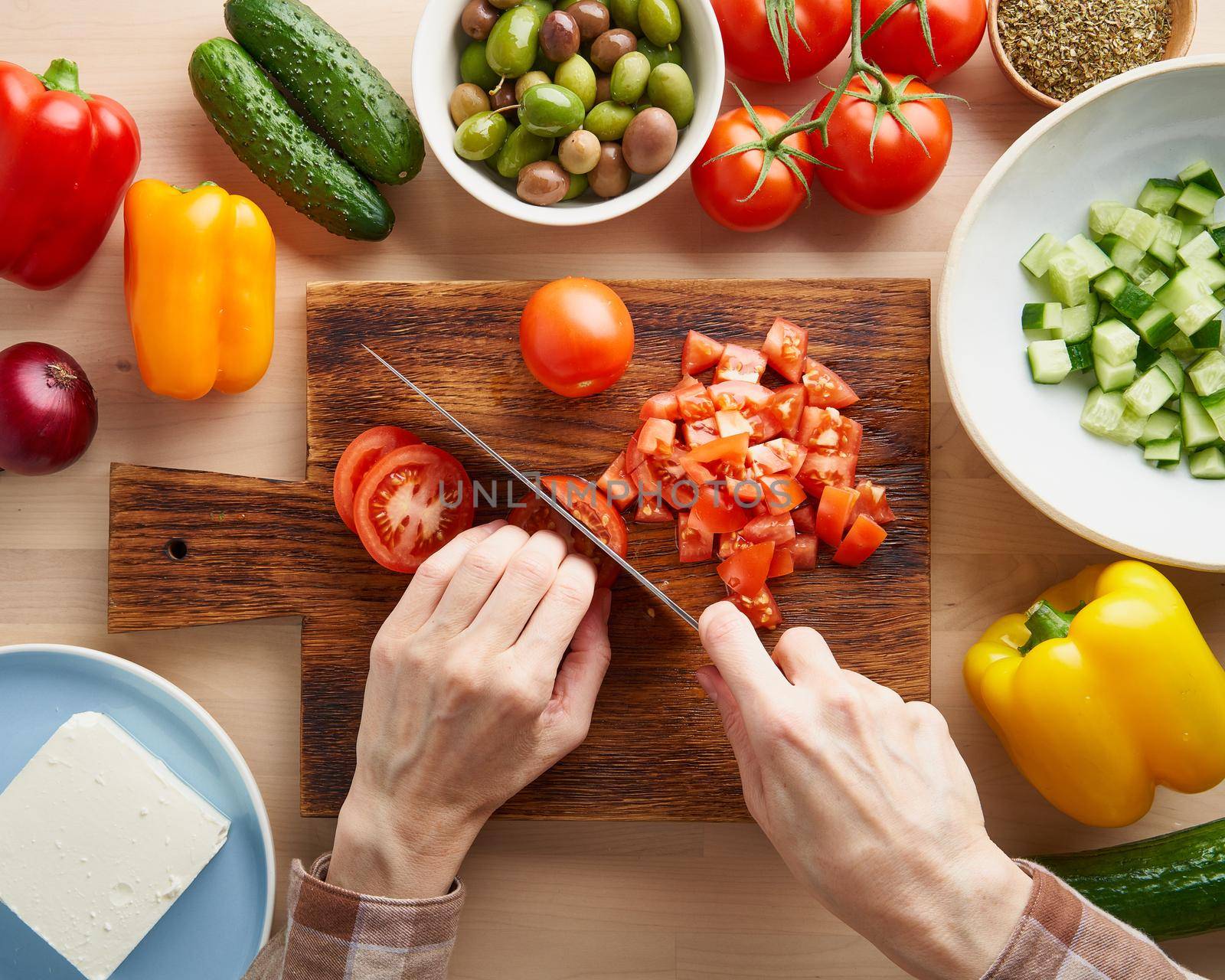 Step by step recipe for salad horiatiki, wooden board for cutting vegetables and ingredients. Hands with knife, chopping tomatoes