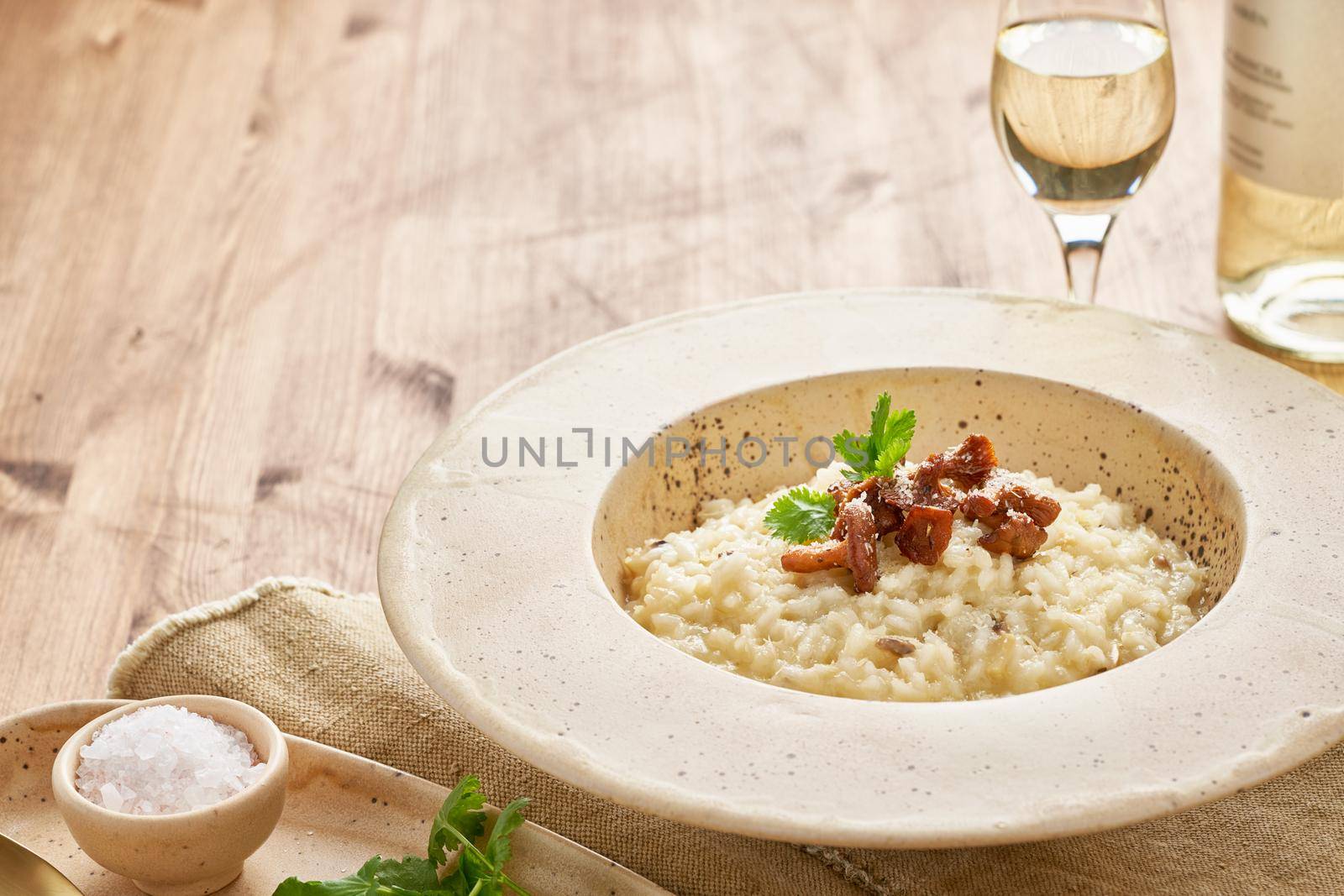 Risoto with chanterelle mushrooms in large plate. Traditional italian dish. Wooden old table, spoons, napkin. Classic hot dish of rice, cheese and wine. Side view, copy space
