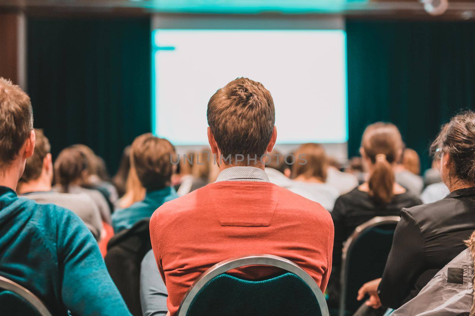 Business and entrepreneurship symposium. Speaker giving a talk at business meeting. Audience in the conference hall. Rear view of unrecognized participant in audience.