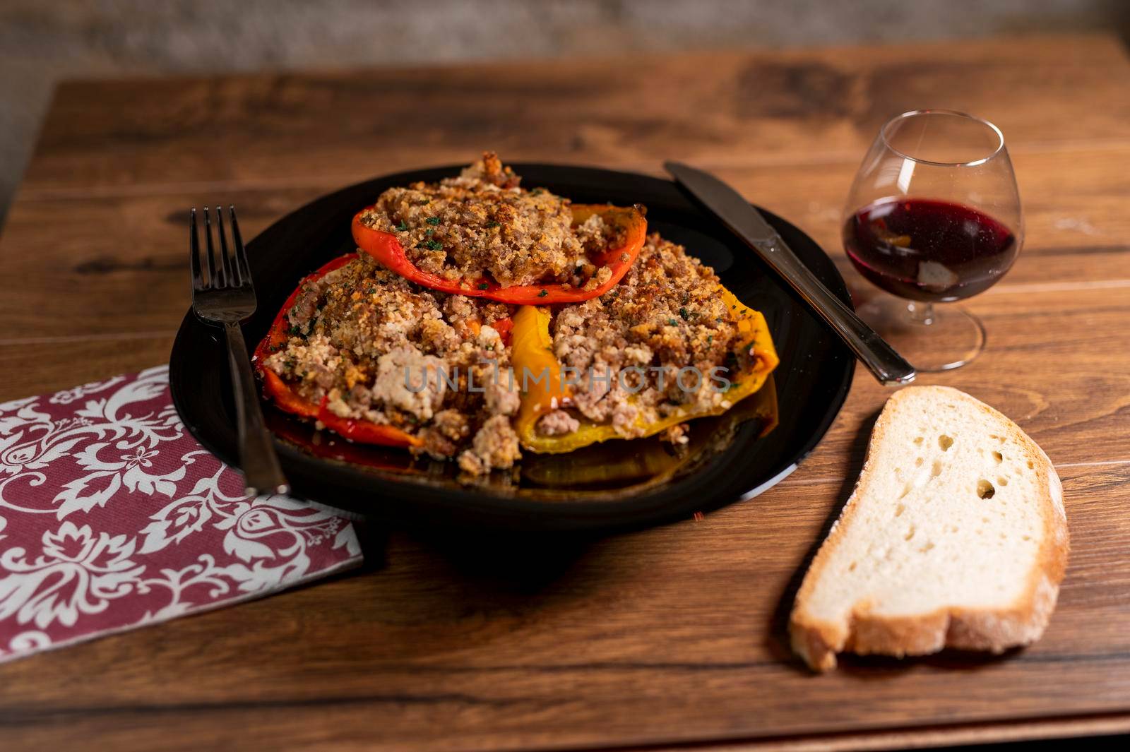 plate peppers au gratin on wooden table with bread cutlery and glass of red wine