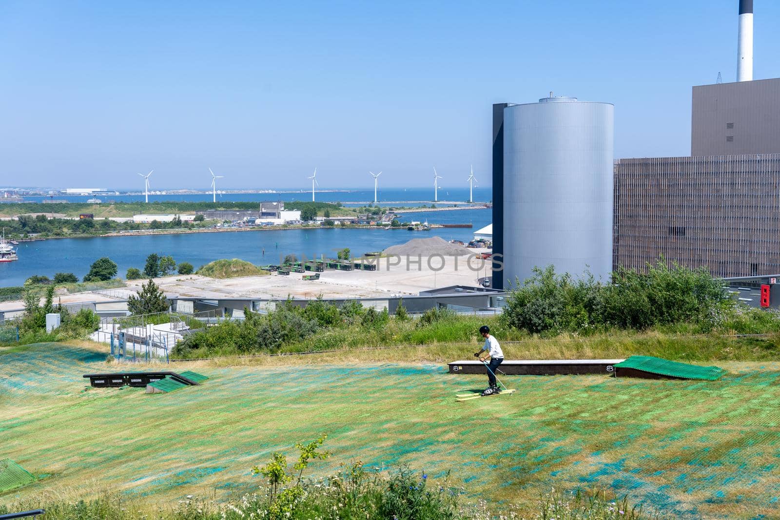 Copenhagen, Denmark - June 18, 2021: Young man skiing down the artificial slope on top of Amager Bakke, a waste to power plant.