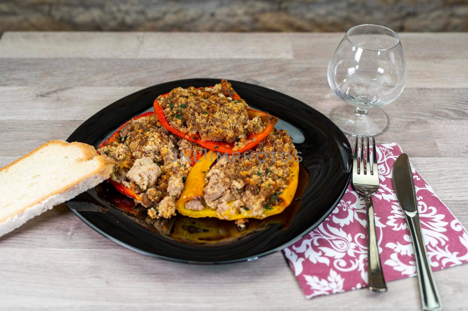 plate of peppers au gratin on wooden table set with cutlery and glass of wine