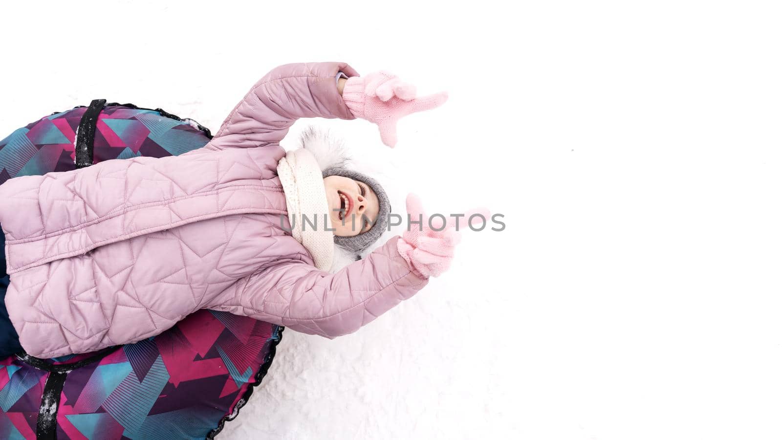 a happy child in winter clothes lies on a colored sled and laughs. place for text. layout for your design. Funny winter sport activity