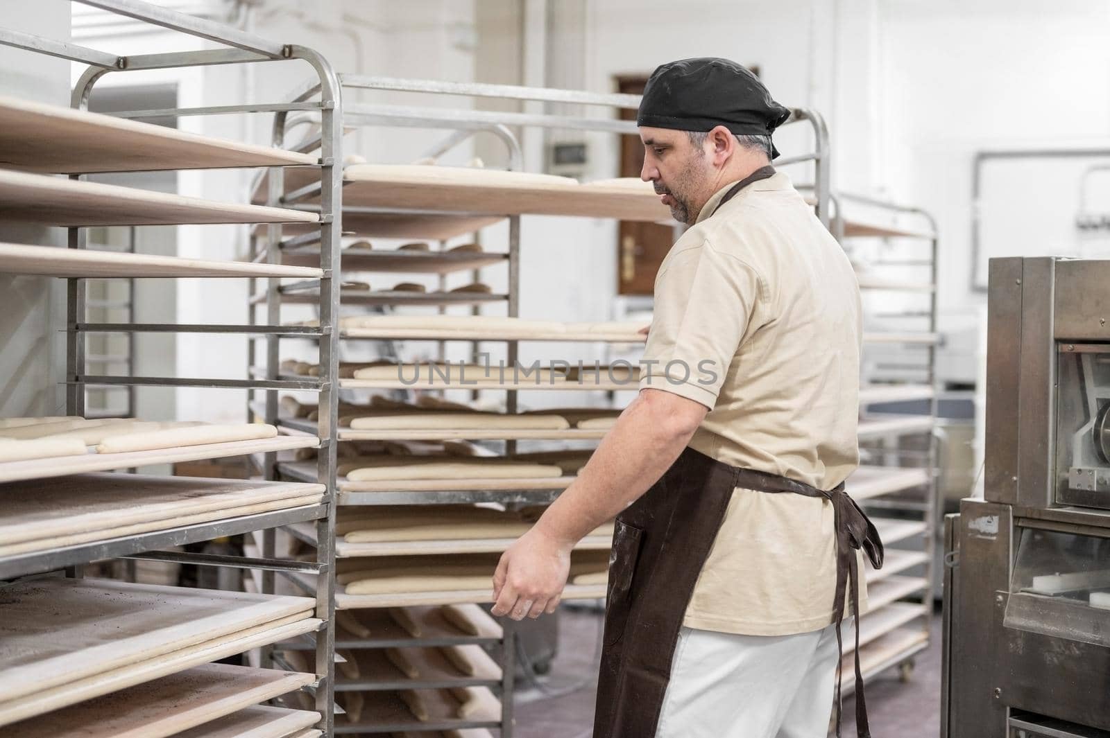 Baker placing tray with formed raw dough on rack trolley ready to bake in the oven by HERRAEZ