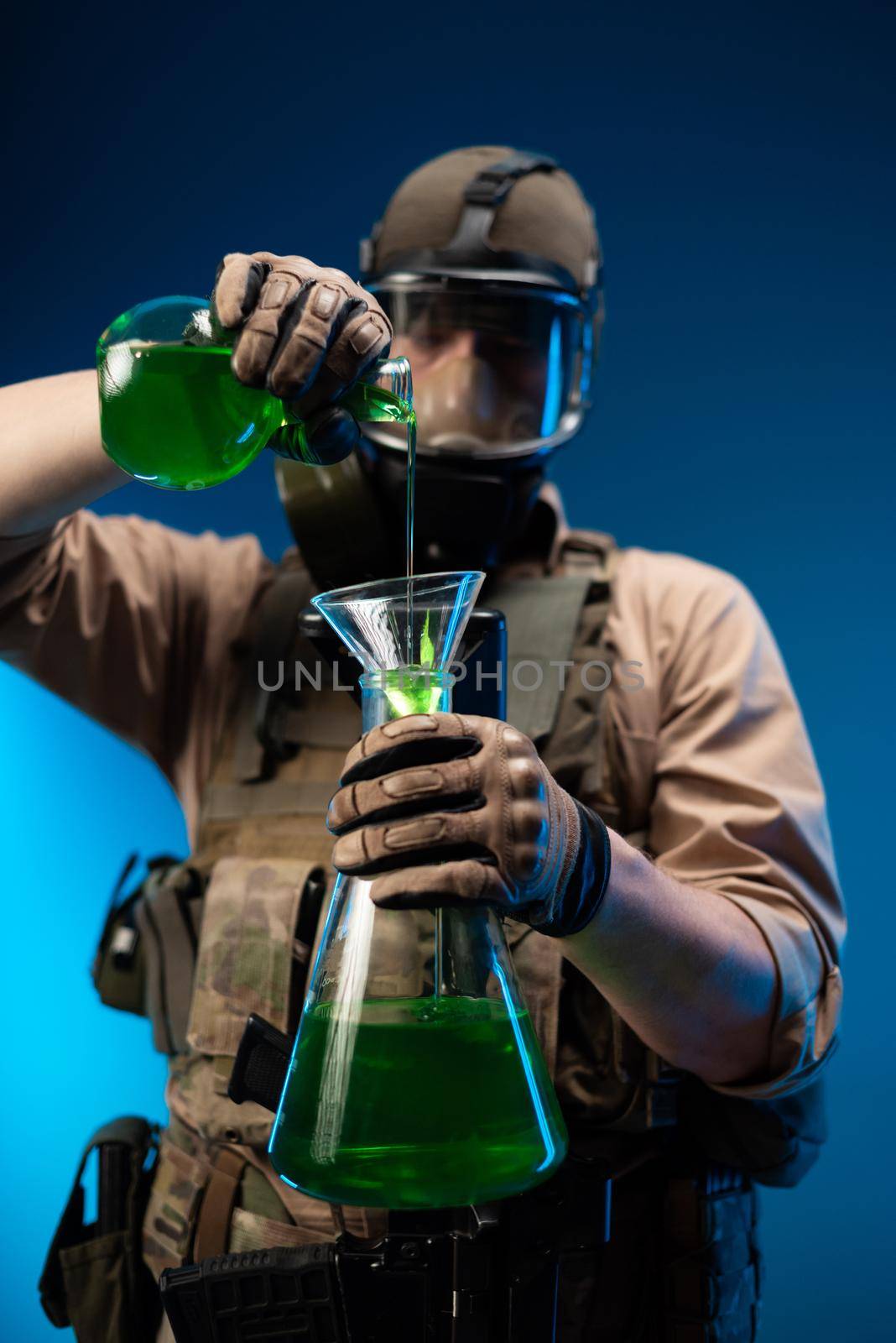 a man in military clothes and a gas mask with laboratory chemical flasks pours reagents by Rotozey