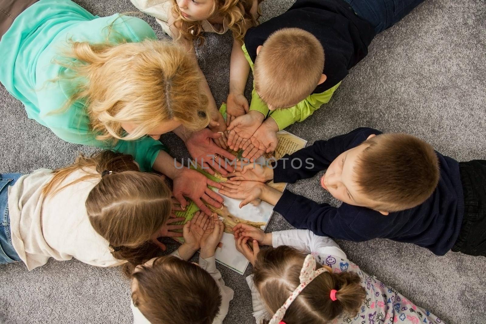 Boys and girls in circle. Happy children having fun. kids lay down together. Happy children lying on the floor in a circle with hands. Top view. Group of children beautiful smile lying on the floor by ViShark