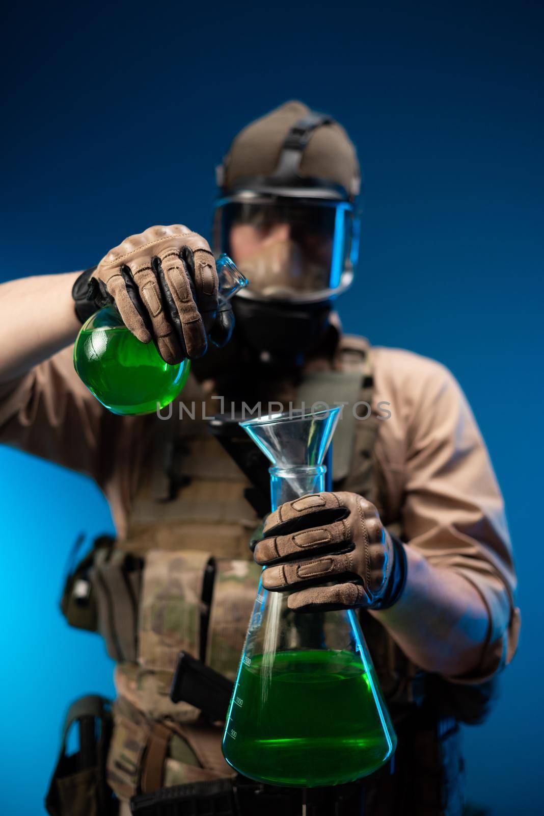 a man in military clothes and a gas mask with laboratory chemical flasks pours reagents