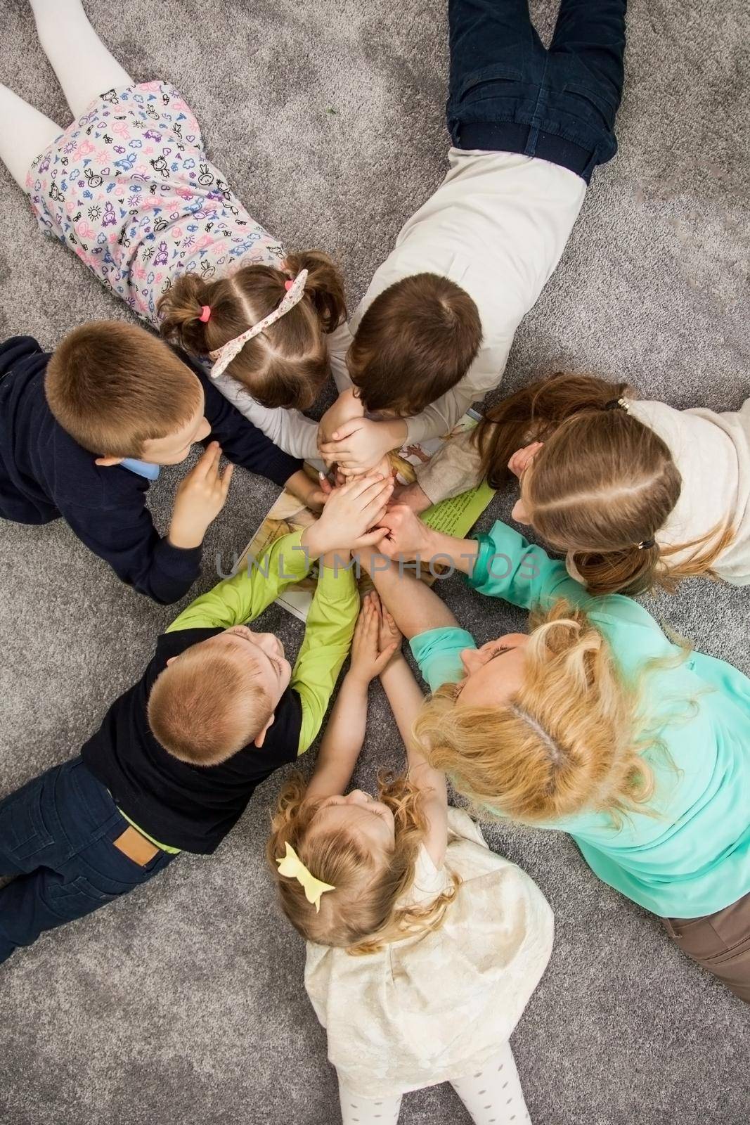 Boys and girls in circle. Happy children having fun. kids lay down together. Happy children lying on the floor in a circle with hands. Top view. Group of children beautiful smile lying on the floor by ViShark