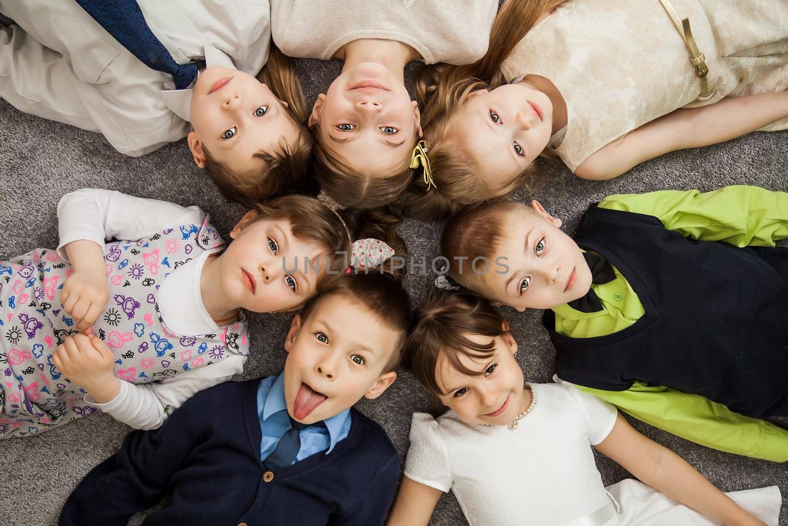 Boys and girls in circle. Happy children having fun. kids lay down together. Happy children lying on the floor in a circle with hands. Top view. Group of children beautiful smile lying on the floor by ViShark