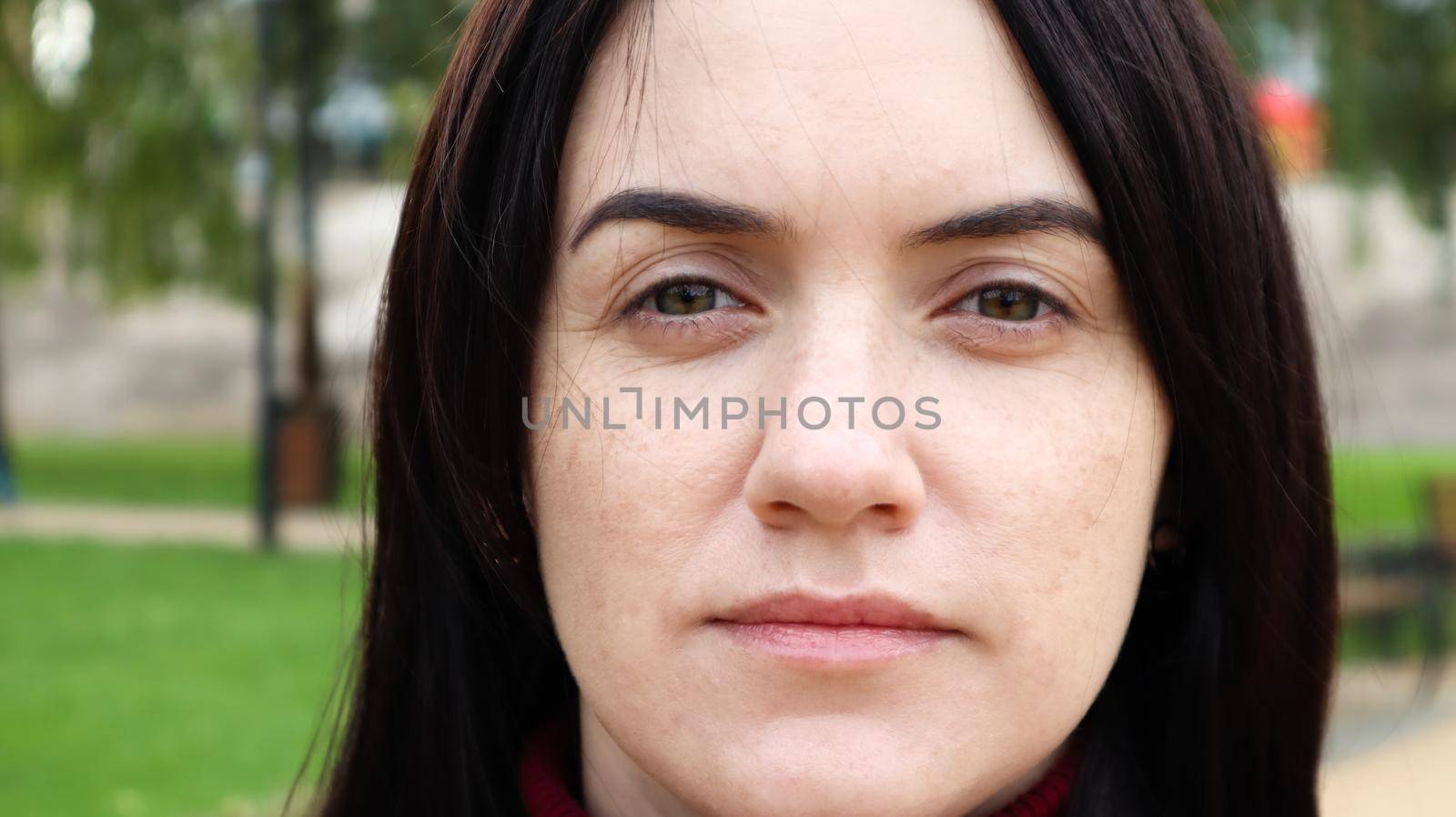 Close up portrait of beautiful caucasian woman while walking outdoors in city park with blurred background. A woman is looking at the camera on a sunny day. by Roshchyn