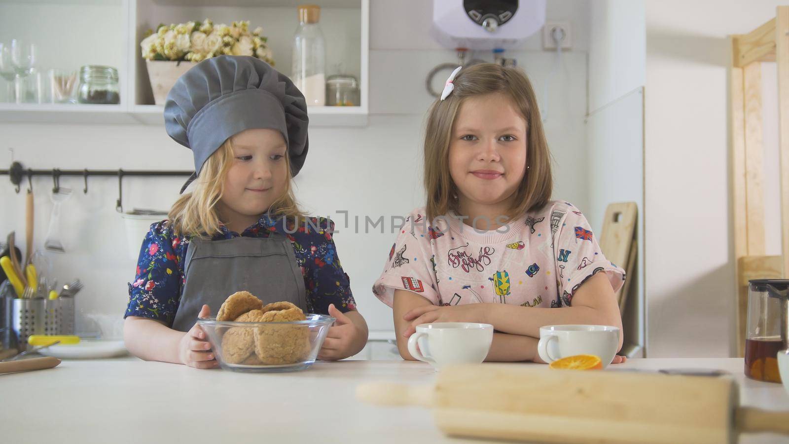 Two little sisters smiling with homemade cookies and cups of tea at cooking studio by Studia72