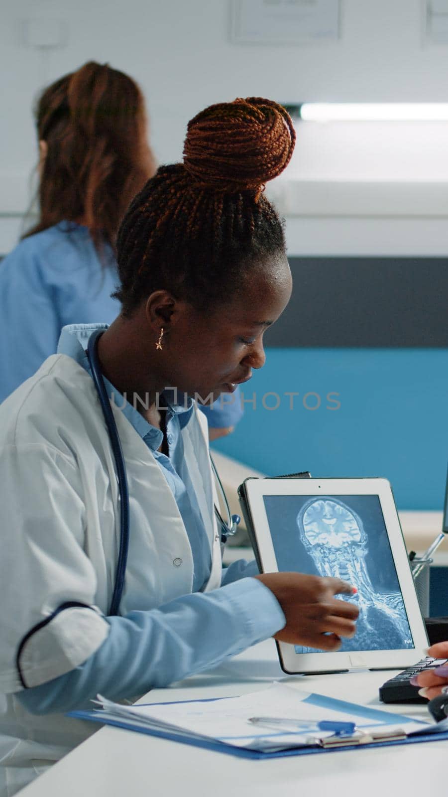 Medic holding x ray scan on tablet for consultation with patient in cabinet. Doctor and ill person looking at gadget screen with radiography for healthcare examination and checkup visit.
