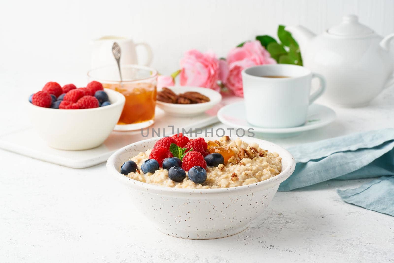 Oatmeal porridge with blueberry, raspberries, jam and nuts in white bowl, dash diet with berries, white background, side view. Healthy diet breakfast