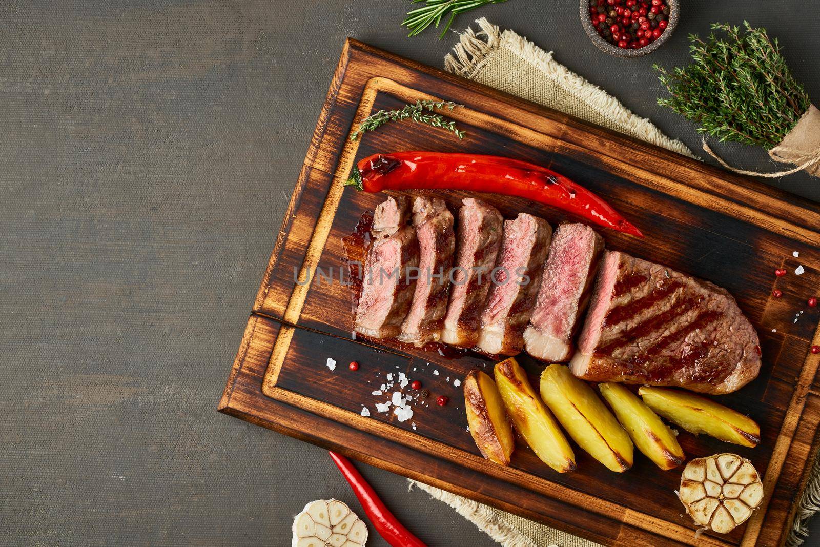 Keto ketogenic diet grilled fried beef steak, striploin, sliced potatoes on cutting board on dark brown table. Paleo food recipe with chopped piece of meat, top view, copy space