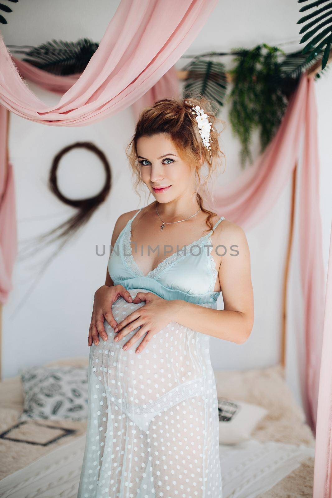 Beautiful blonde woman in pregnant, wearing in night dress and lace lingerie, posing inside big rounded decoration with flowers. Sensuality and beautiful mom. Pregnant period. Stylish interior.