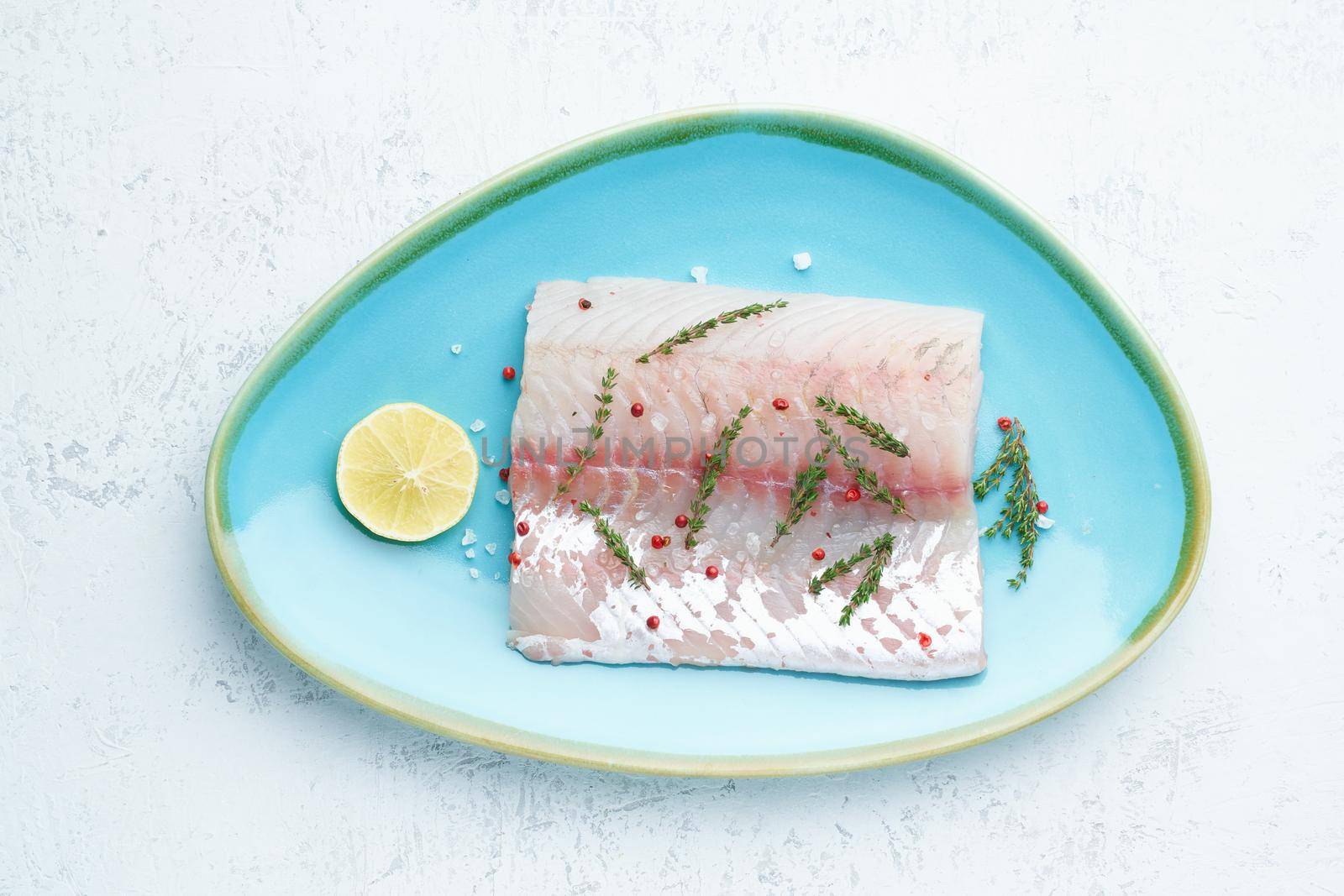 Fillet of raw white walleye fish on a blue plate on a white background. Whole piece of fresh fish with herbs and lemon. Top view