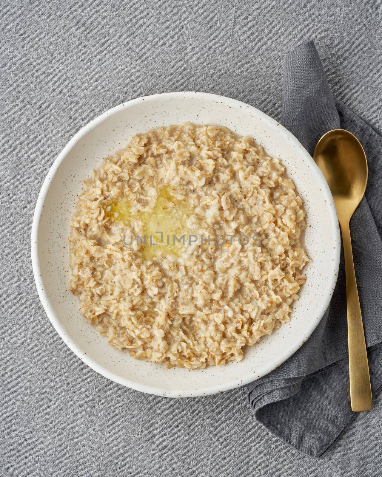 Whole oatmeal, large bowl of porridge with butter for breakfast, morning meal. Top view, close up, gray table. Vegan tasty healthy diet. Vertical