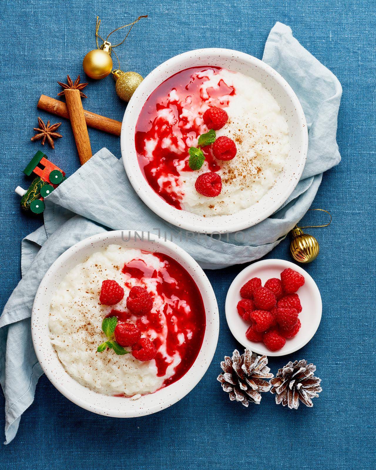 Rice pudding. Christmas food. French milk rice dessert with raspberries, blueberries, berries, jam. Healthy Vegan diet breakfast with coconut milk, cinnamon. Blue linen textile. Dark background.