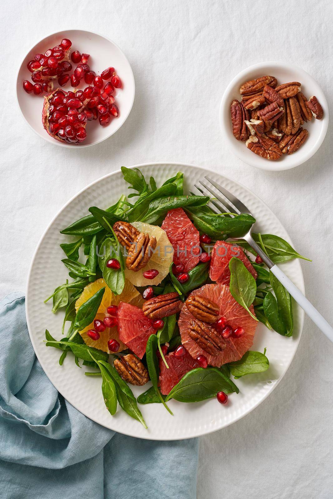 Top view of Fruits citrus salad with nuts, green lettuce leaves. Balanced food. Spinach with orange, grapefruit, pecans and pomegranate seeds in bowl on table with white tablecloth.