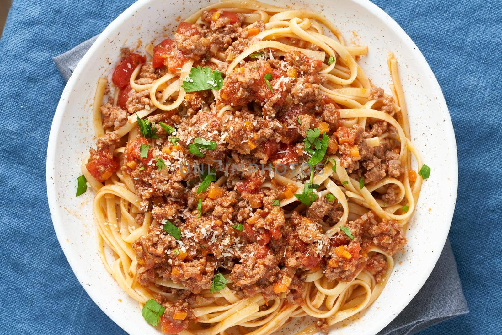 Pasta Bolognese Linguine with mincemeat and tomato sauce, parmesan cheese, parsley. Italian dinner, dark blue tablecloth. Top view, close up