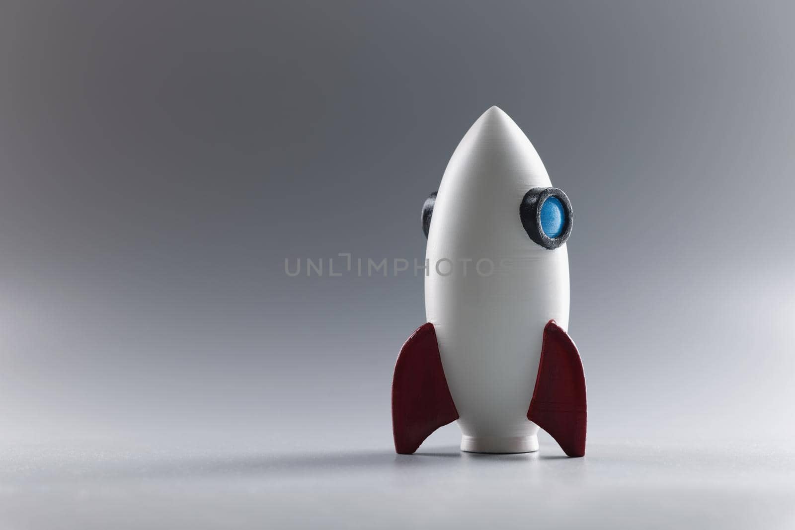 Close-up of rocket toy model stand on grey surface, rocketship as symbol for business project or startup. Success, growth, development concept. Copy space