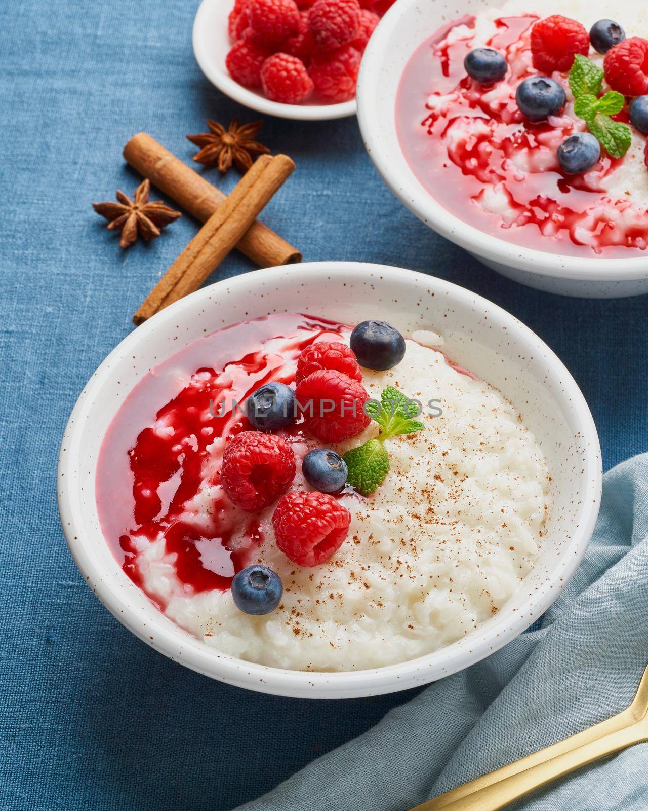 Rice pudding. French milk rice dessert with raspberries, blueberries, berries, jam. Healthy Vegan diet breakfast with coconut milk, cinnamon. Blue linen textile. Dark background.