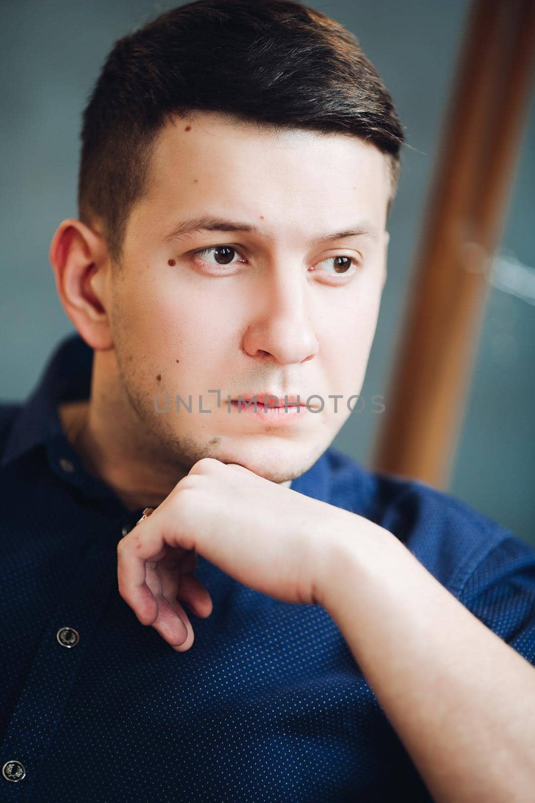 Close up of portrait of confident boyfriend seriously looking at side and thinking. Brunet male touching chin by hand. Studio background.