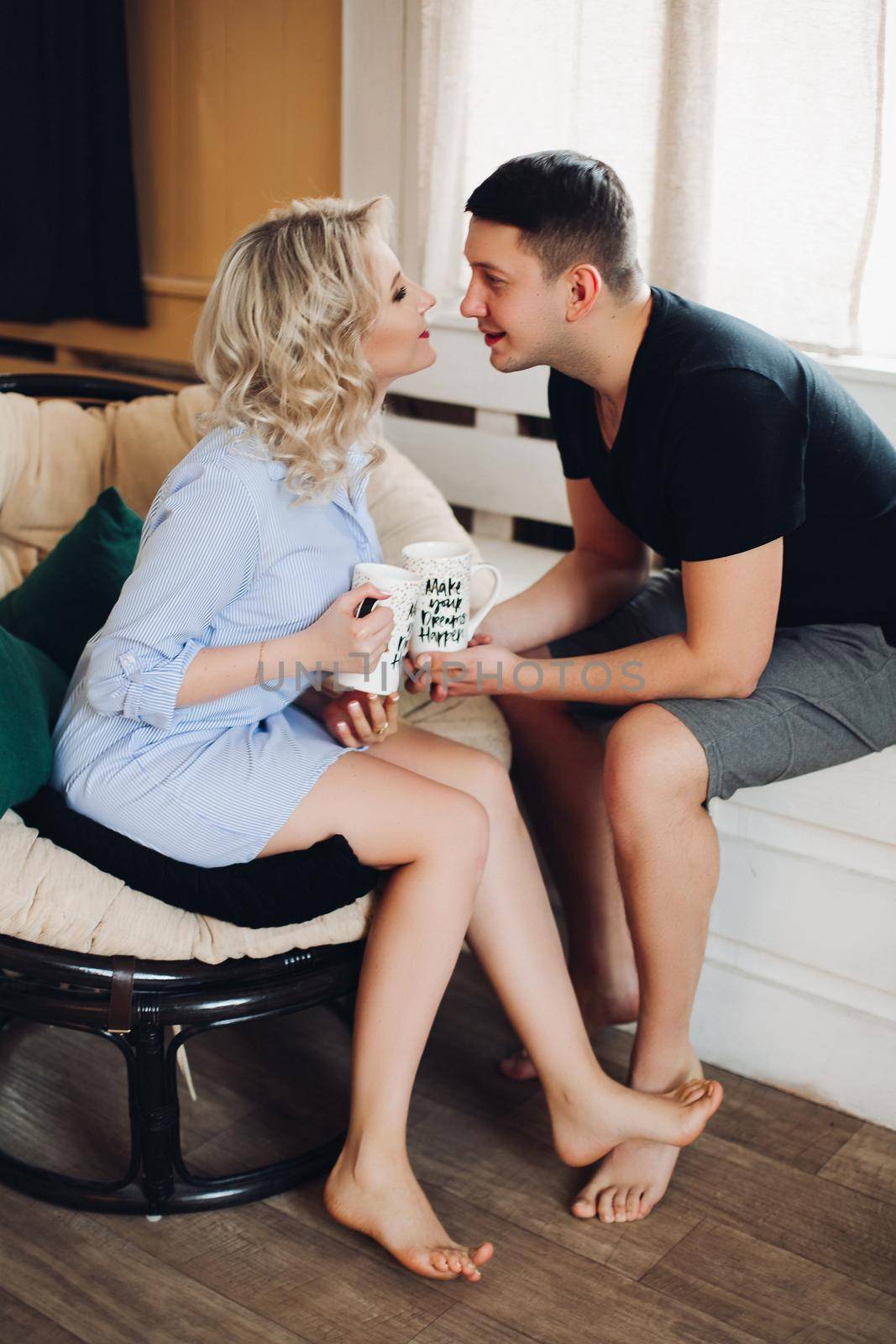 Close up of young sweet couple in love. Blonde girl in striped shirt and a man in black tshirt kissing tenderly,holding in their hands cups with creative inscription.Concept of love and relationship.