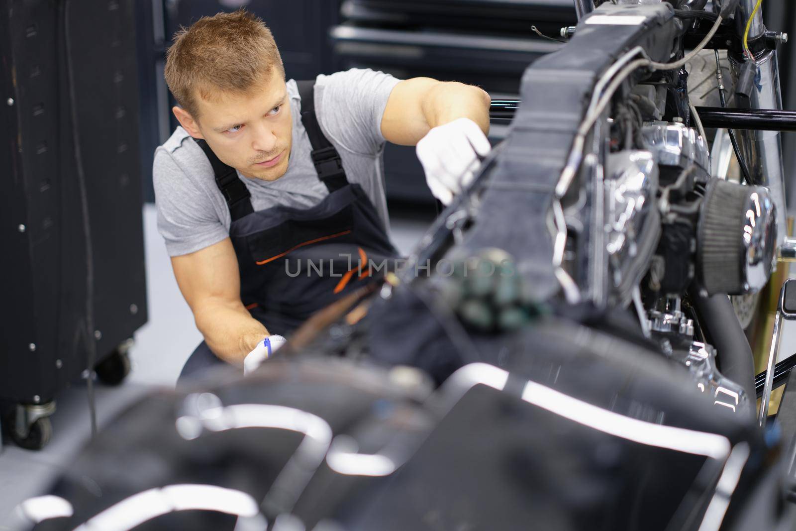 Portrait of concentrated serious handyman with tool fix damaged motorbike in garage. Mechanic work in gloves. Pit stop, service help, maintenance concept