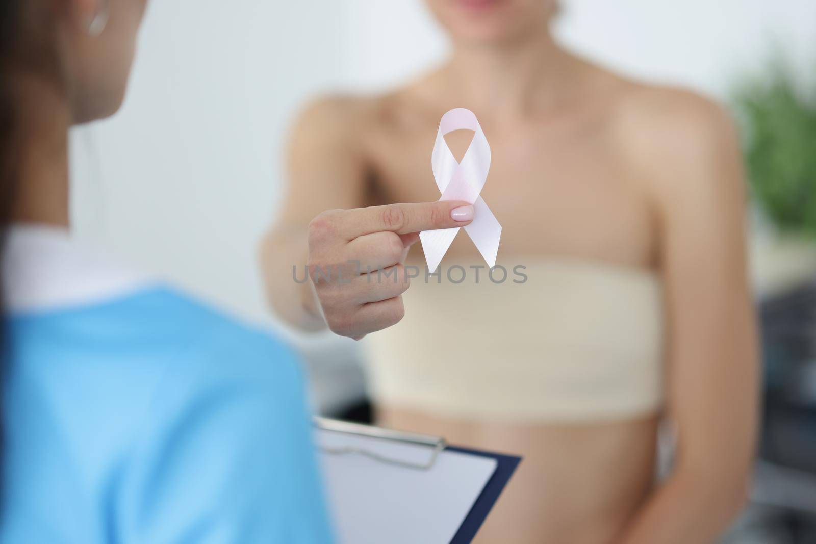 Close-up of female show white ribbon sign, symbol for breast cancer. Woman patient on doctor consultation in hospital. Medicine, healthcare, ill concept