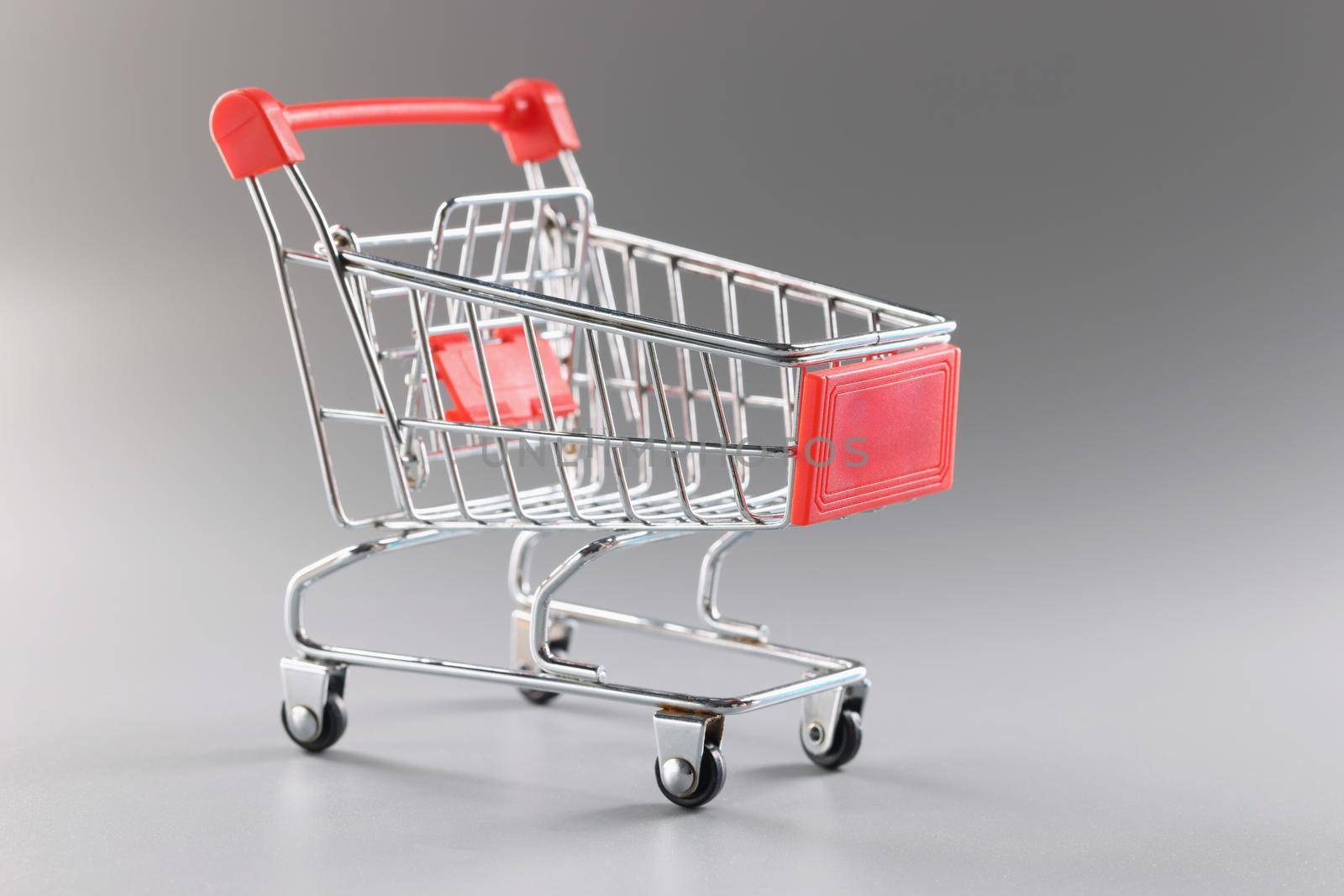 Close-up of empty shopping cart against grey background, single miniature model of container to collect products. Shopping, grocery, food, storage concept