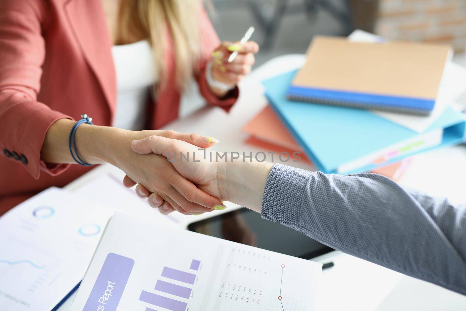Close-up of partners shake hands over business papers on workplace in office. Biz partners perform friendly gesture after agreement. Deal, contract concept