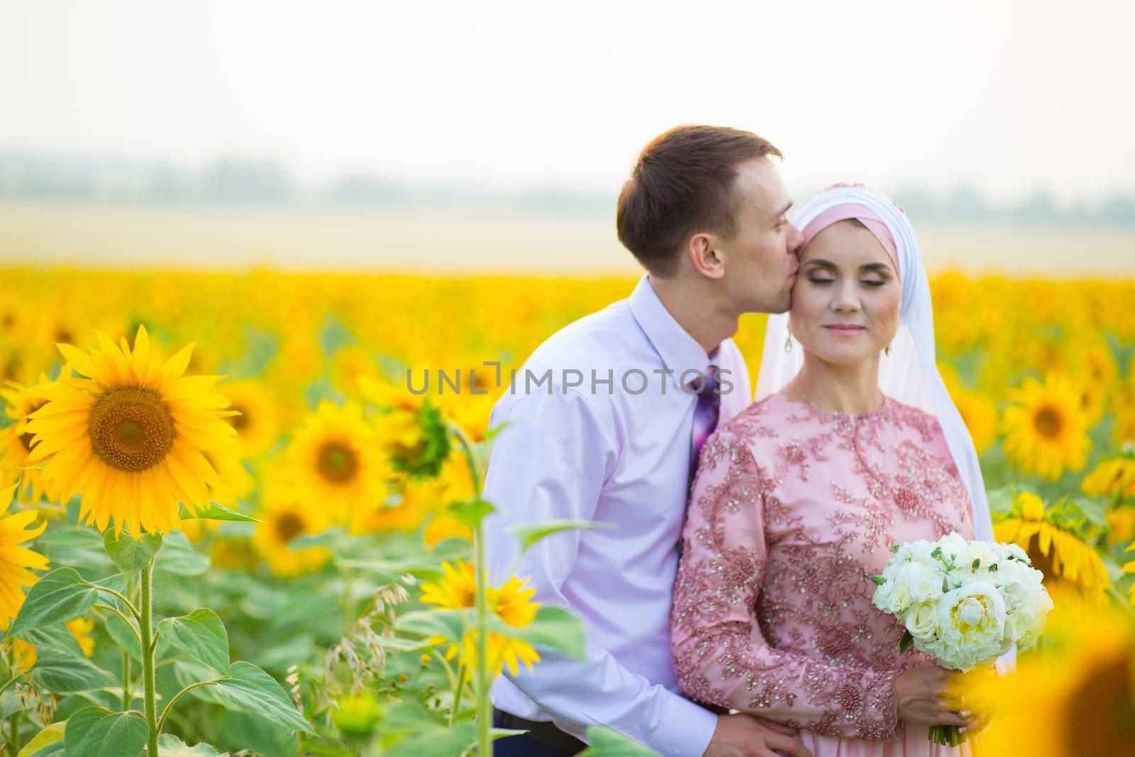 Smiling young islamic couple portrait on sunflowers field. Muslim marriage.
