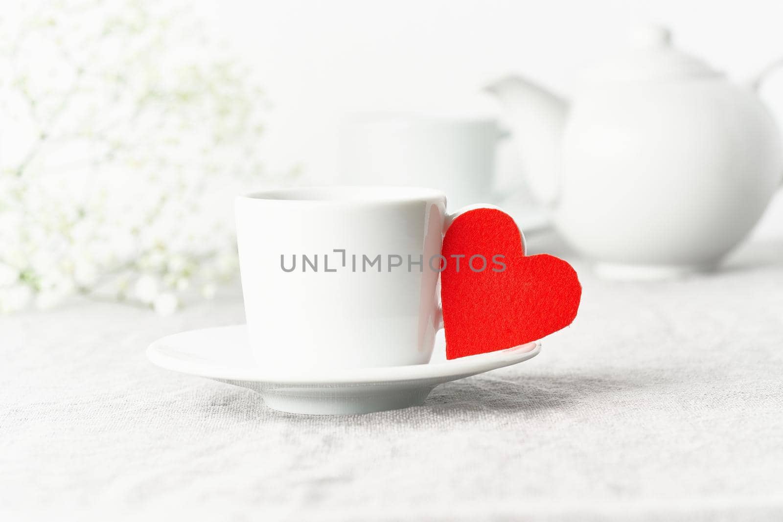 Valentine's Day. Morning breakfast for two with tea and flowers. Red felt heart is symbol of lovers. Light white tender pastel background. Scandinavian minimalism. Side view, copy space