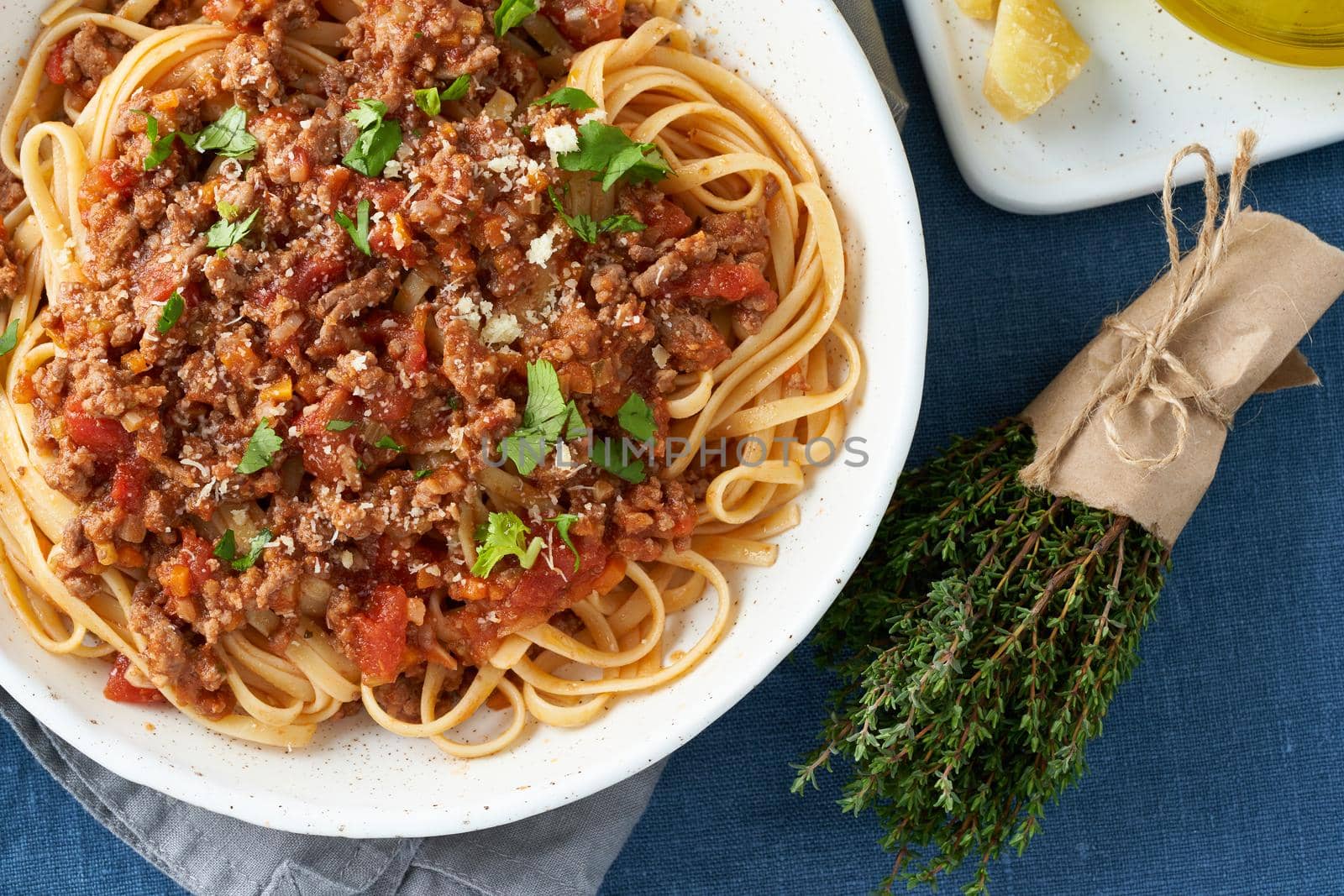 Part of pasta Bolognese Linguine with mincemeat and tomatoes, parmesan cheese. Italian dinner for two, dark blue tablecloth. Top view, close up