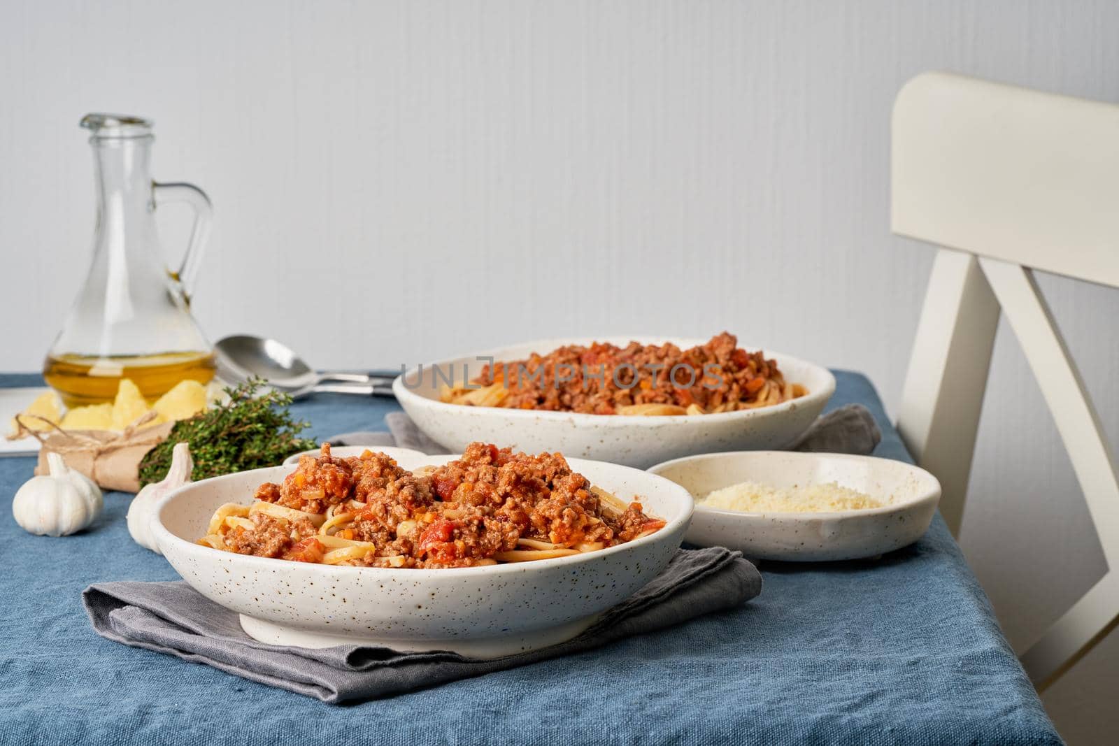 Pasta Bolognese Linguine with mincemeat and tomatoes. Italian dinner for two at the table, dark blue tablecloth, chair, homeliness. Side view
