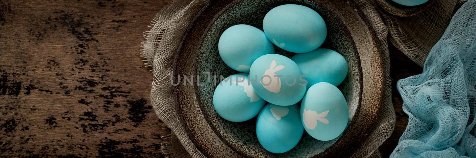 Banner with unusual Easter on dark old background. Ceramic brown bowl with blue eggs with rabbit. by NataBene