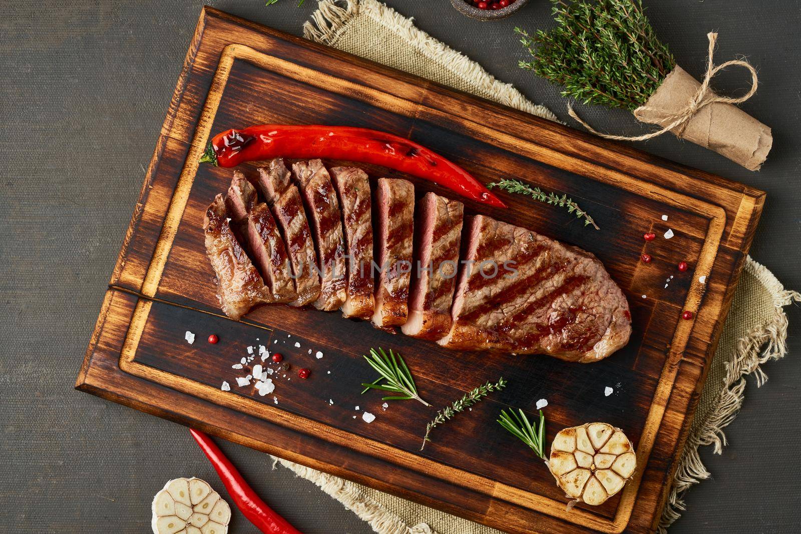 Keto ketogenic diet beef steak, well done grilled fried striploin on cutting board on dark brown table. Paleo food recipe with chopped piece of meat, top view, copy space