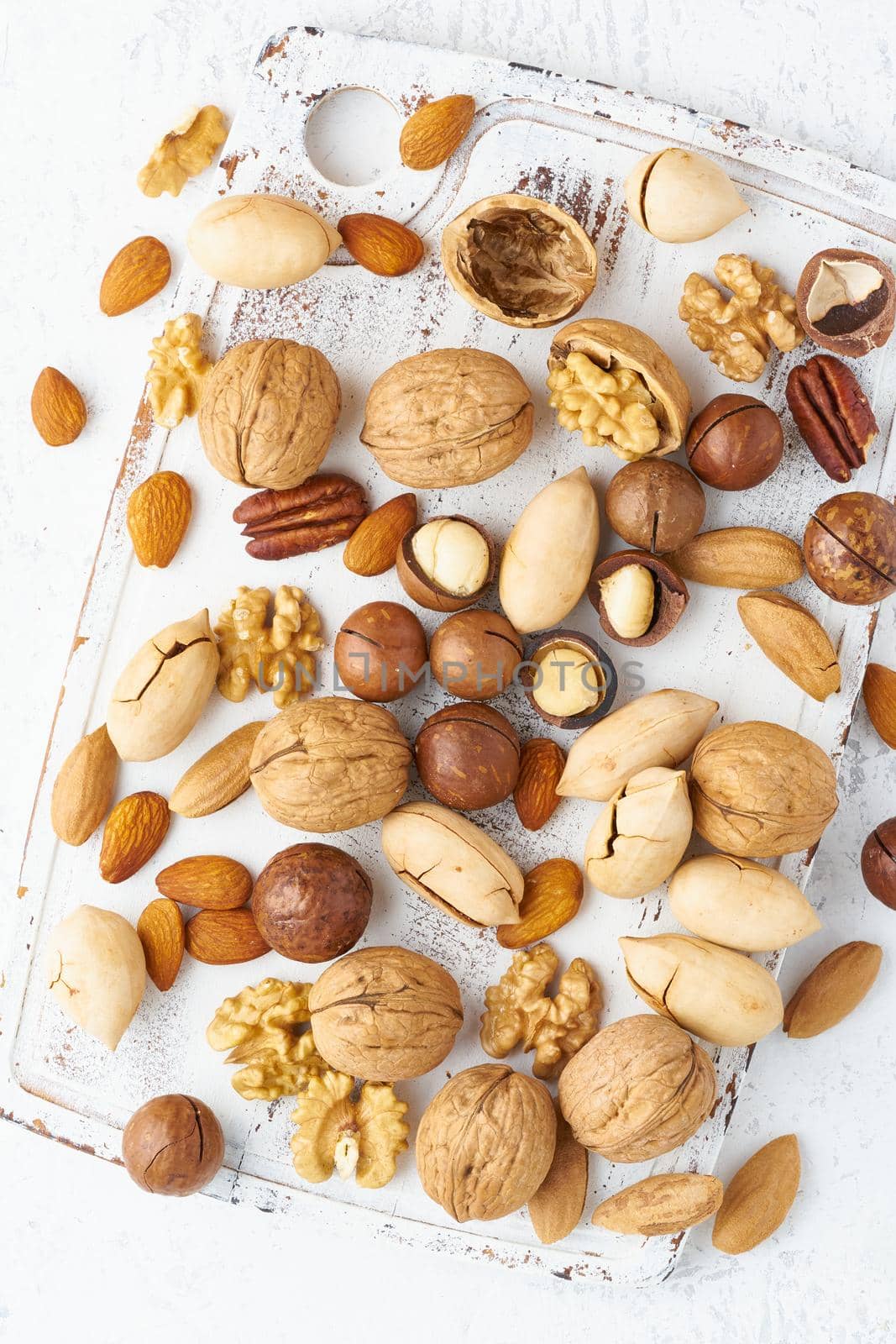 Mix of nuts - walnut, almonds, pecans, macadamia and knife for opening shell on a white wooden cutting board. Healthy vegan food. Clean eating, balanced diet. Top view, macro, close up